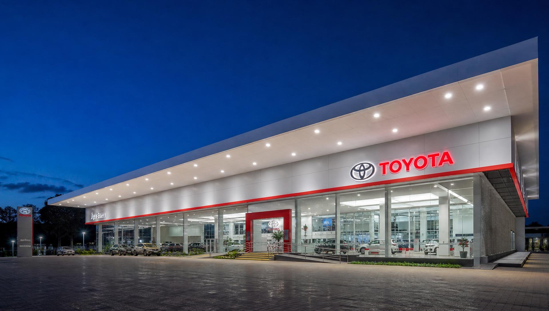Fachada completa de concessionária Toyota de alto padrão com pátio discreto de veículos ao fundo
