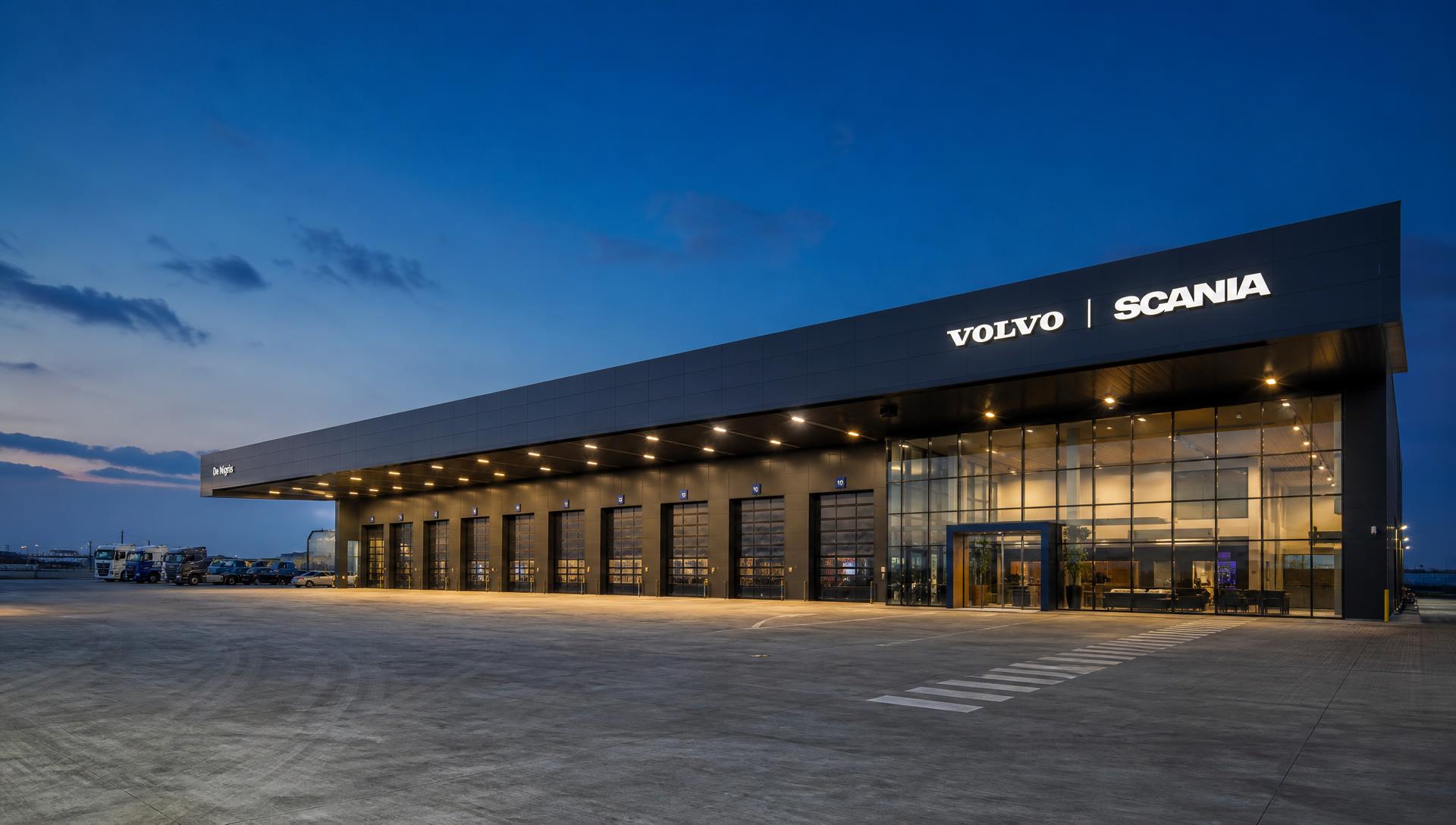 Fachada completa de concessionária Volvo e Scania com boxes técnicos e pátio operacional ao fundo
